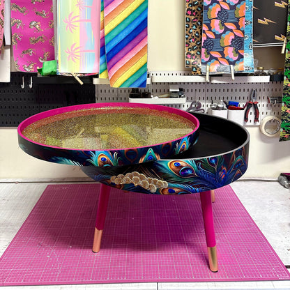 Round coffee table , peacock design, blue, teal and turquoise feathers. Bright pink. Round table, lift off top for storage. End table lounge